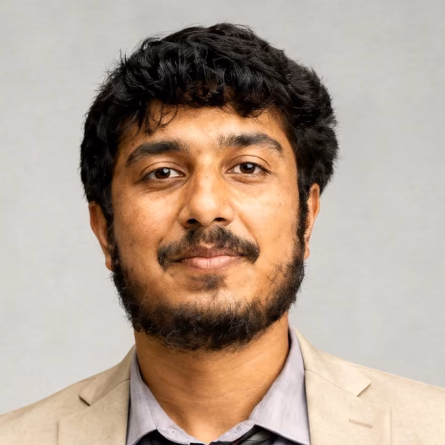 Portrait of a man with curly black hair, beard, and mustache wearing a beige blazer and gray shirt.
