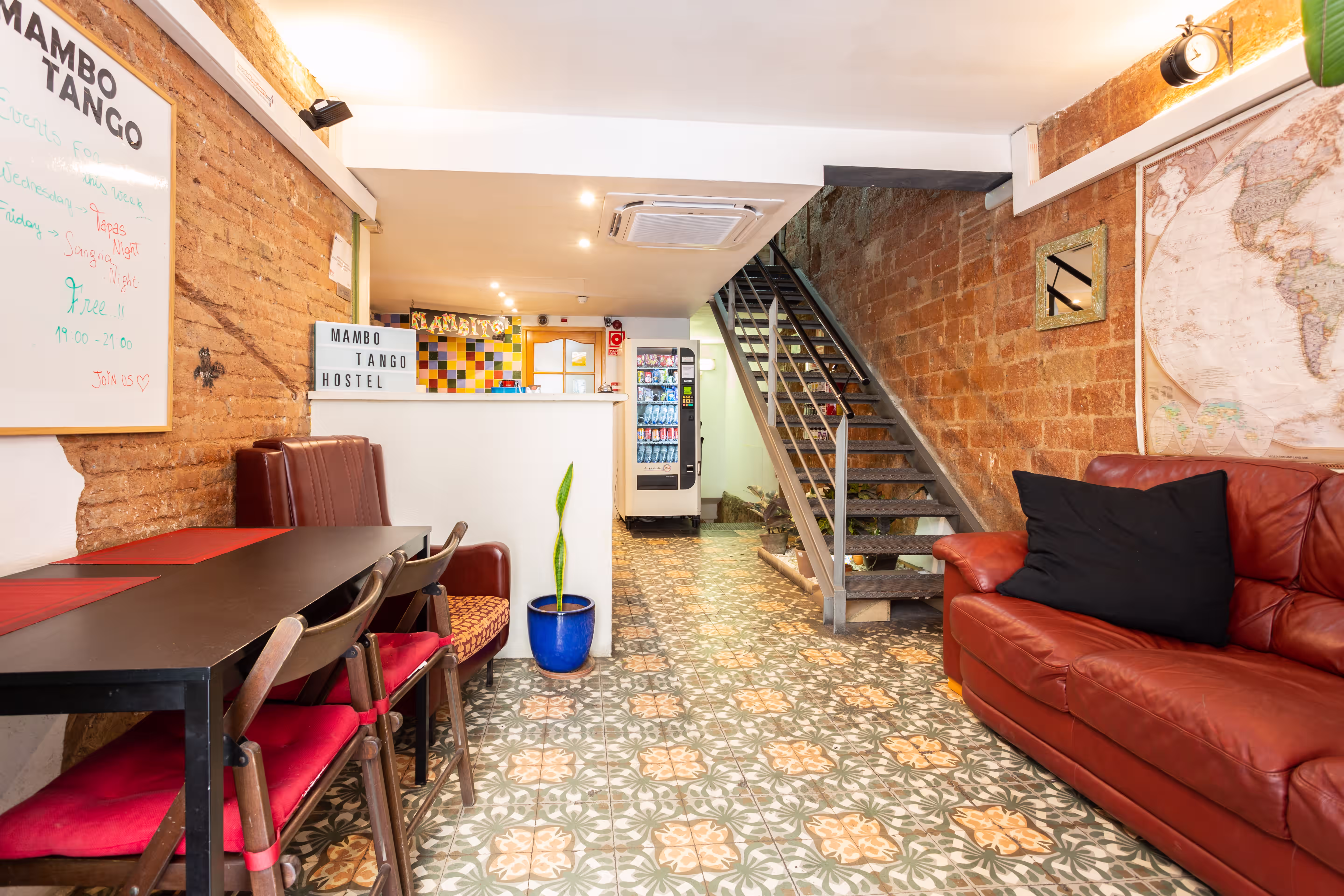 Hostel lobby with patterned tile floor, red leather couch, stairs, vending machine, and seating area.