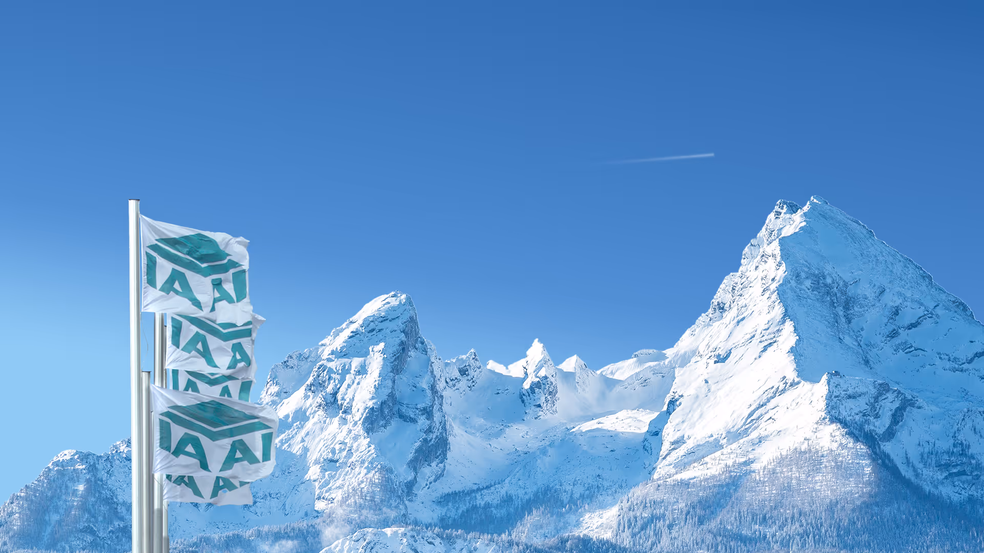 Drei Fahnen mit IAA-Logo wehen vor verschneiten Bergen unter blauem Himmel.