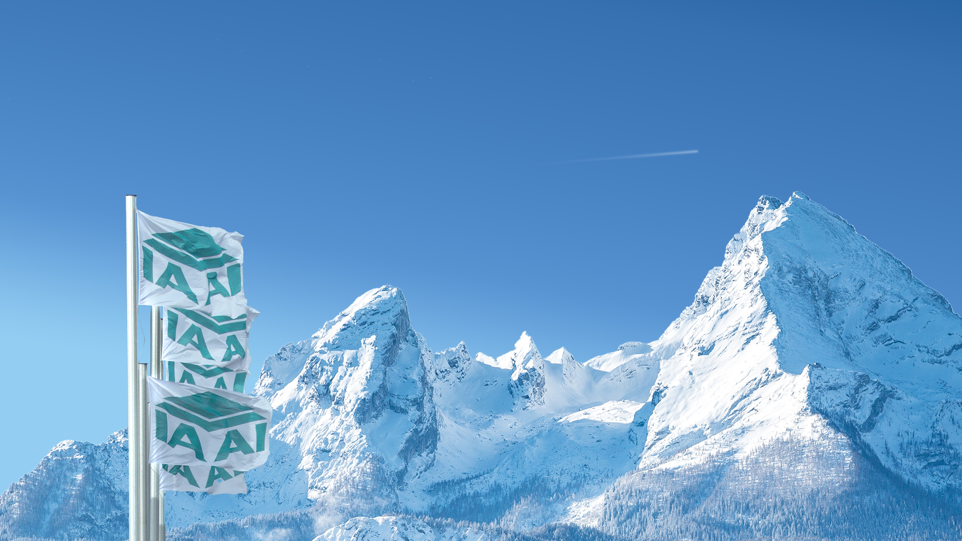Drei Fahnen mit IAA-Logo wehen vor verschneiten Bergen unter blauem Himmel.