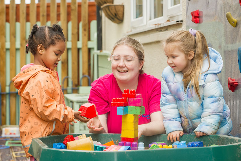 Smiling Nursery teacher playing outside with 2 children