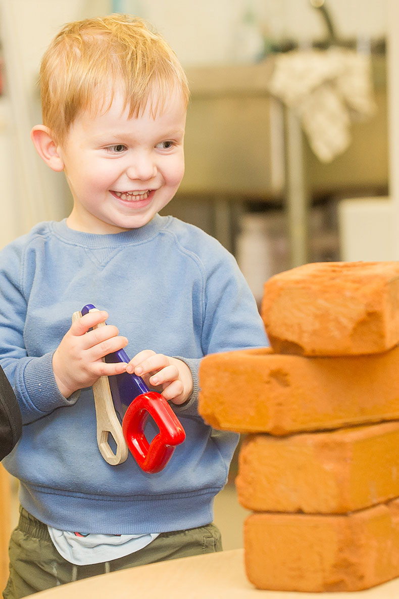 Smiling boy in blue top holding plastic saw and spanner