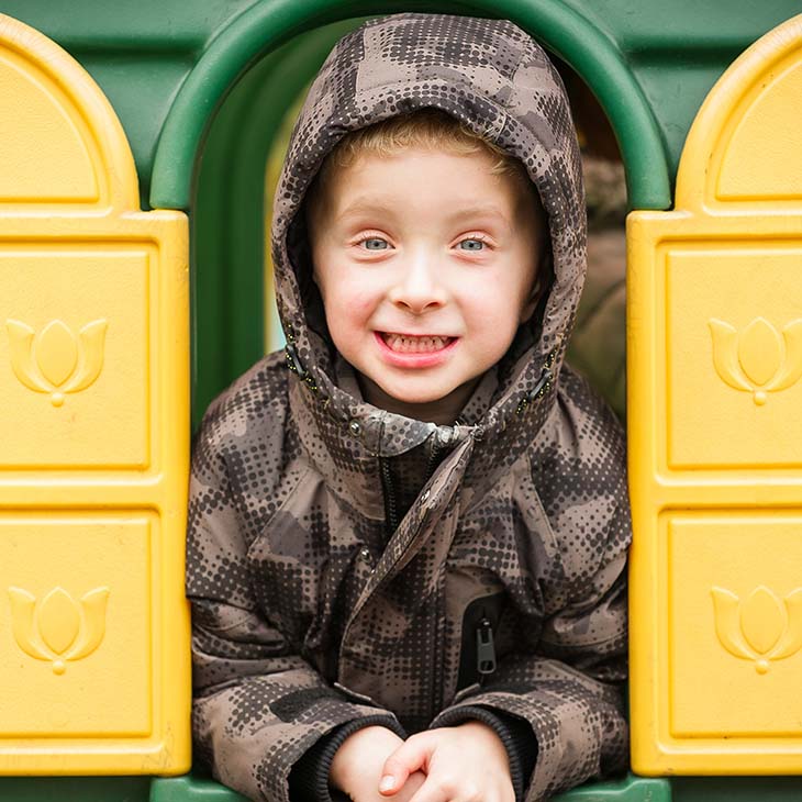 Boy in coat peeping out of outside playhouse
