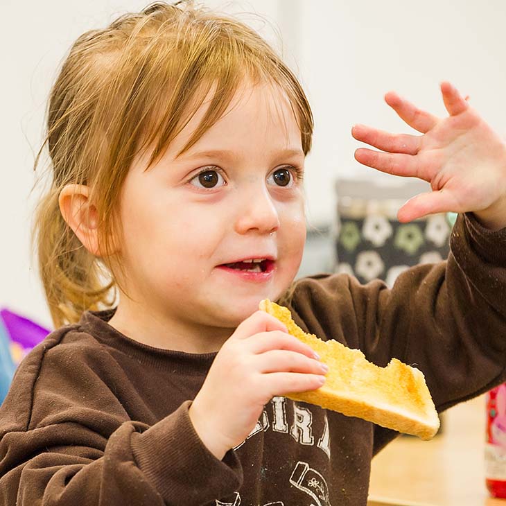 Waving little girl eating a piece of toast