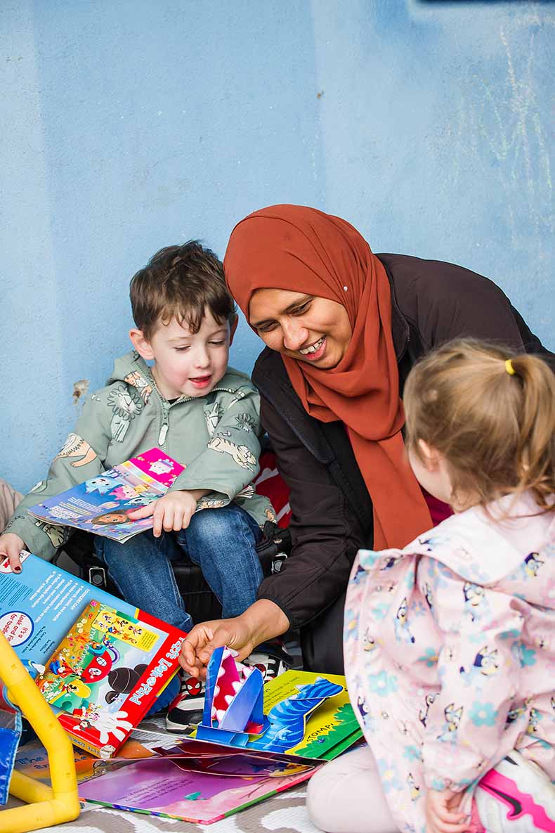 Smiling nursery teacher reading a story to 2 children