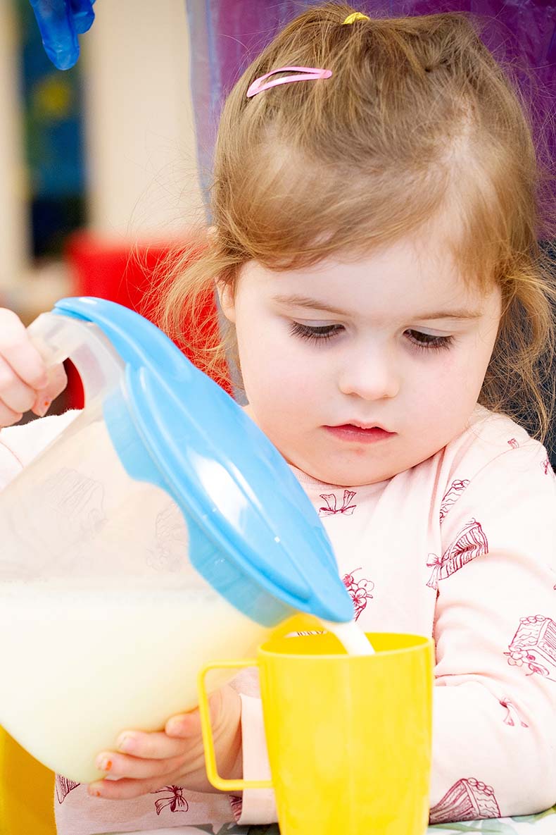 Little girl pouring water from a jug into a cup
