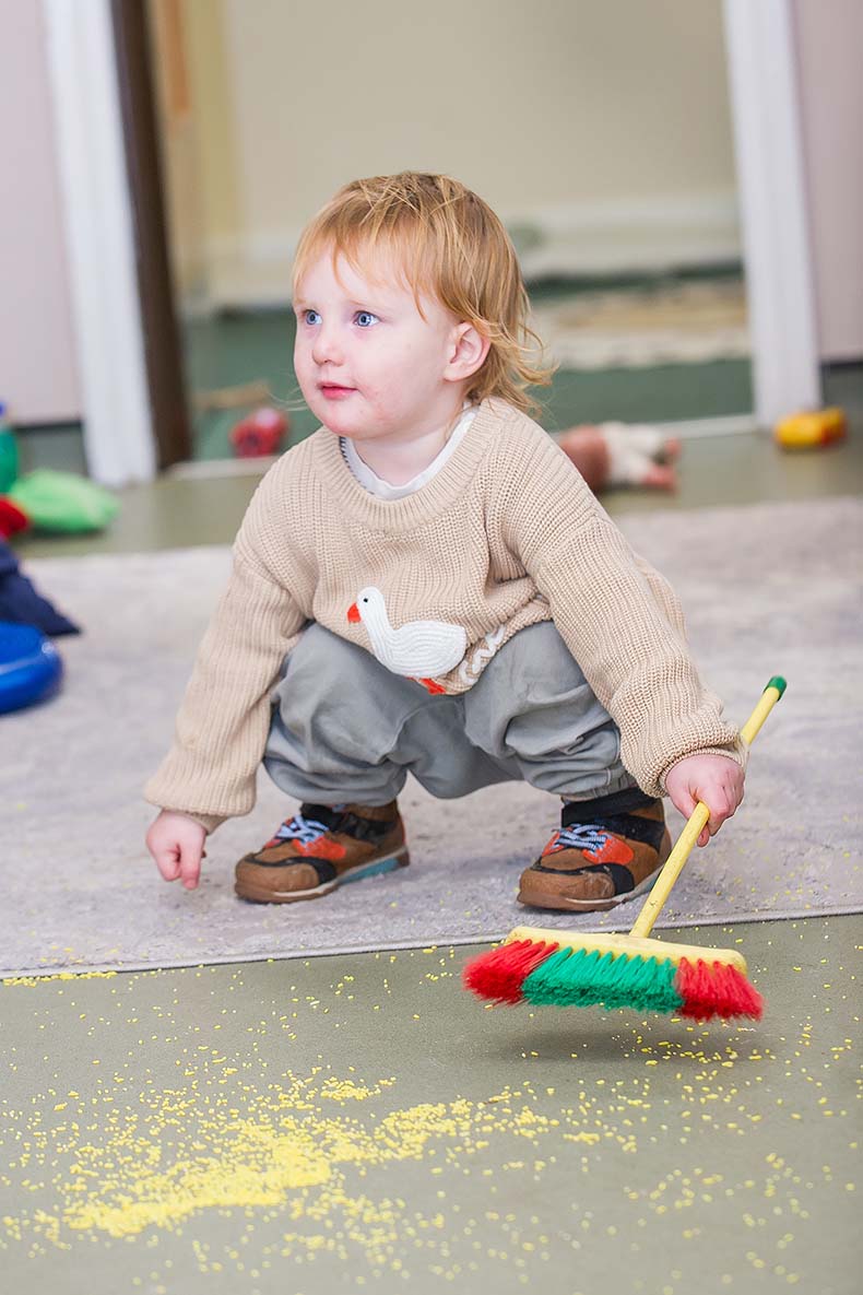 Little boy crouching down with a broom in his hand