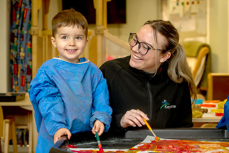 Smiling nursery teacher painting with a little smiling boy