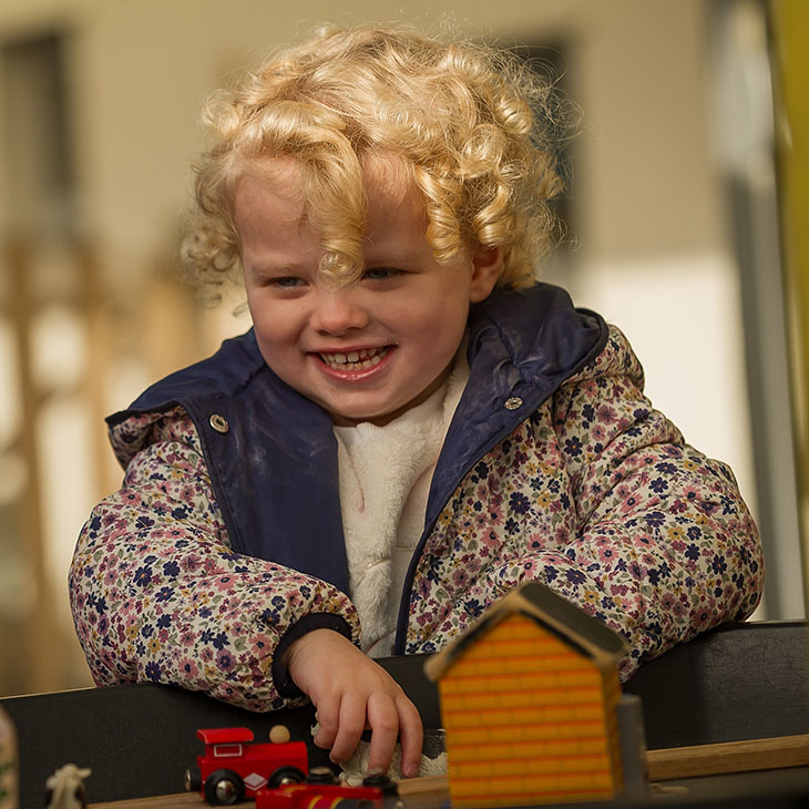 smiling girl playing with wooden train set