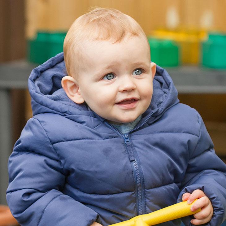Little boy in blue coat riding plastic toy car