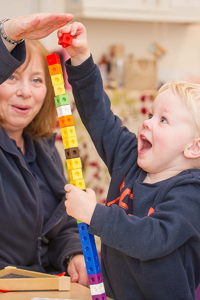 Little boy building a huge lego tower with teacher looking on