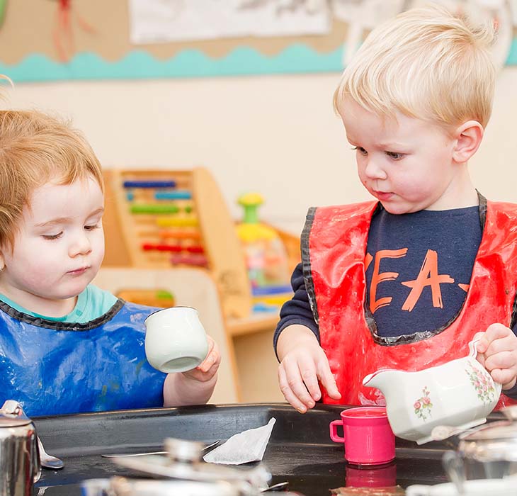 Two toddlers with aprons playing with water