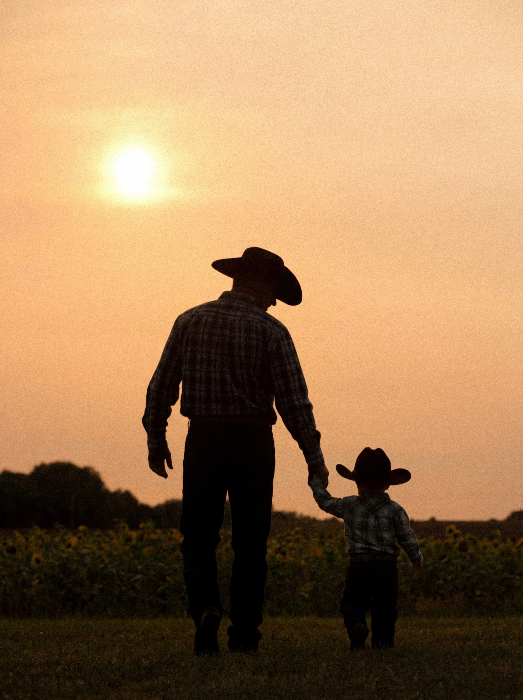 A father and child in cowboy hats walking hand in hand at sunset