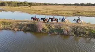Horses and riders follow a path between pools of water.