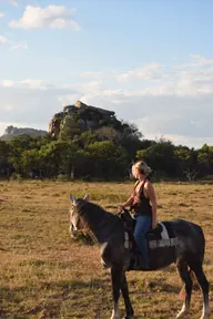 A rider and grey horse beside rocky outcrops.