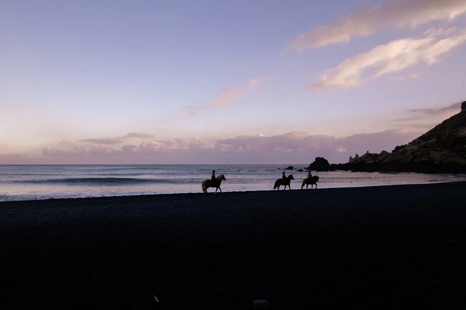 Three riders on Icelandic horses along South Iceland's black sand beach at sunset.