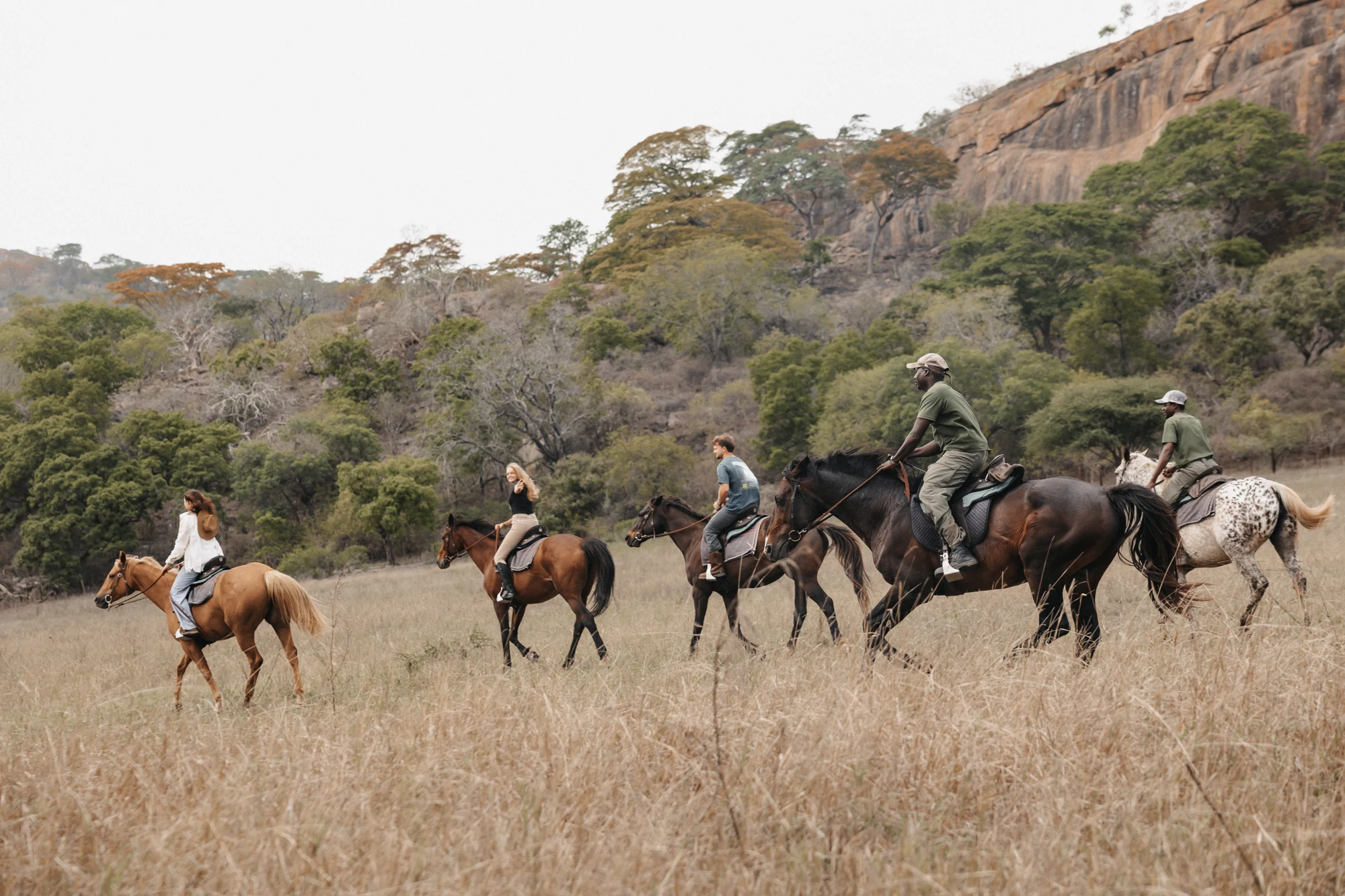 A group riding horses beneath the rocky hills of a reserve in Zimbabwe