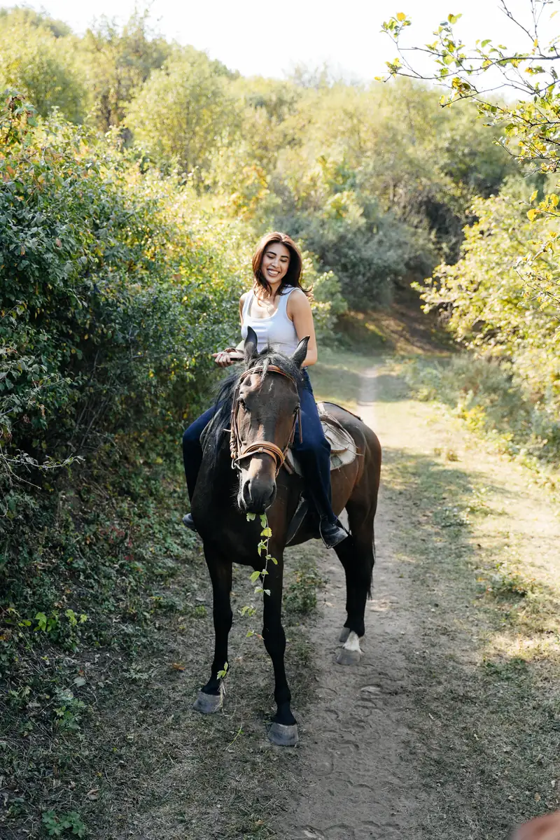 A smiling rider on a dark horse along a leafy path near Almaty.