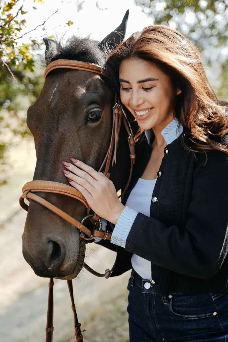 A smiling woman resting her hand on a brown horse’s face.