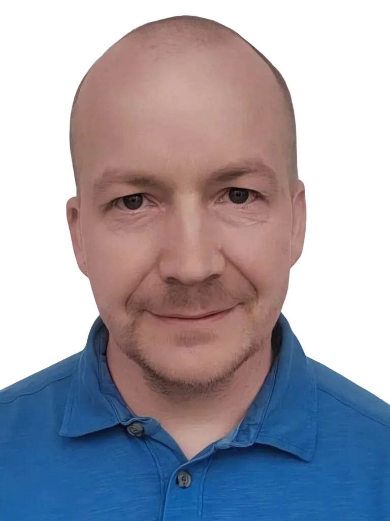 Lähikuva kaljusta, vaaleaihoisesta miehestä, jolla on tummat silmät ja kevyt parta. Hän hymyilee hieman ja pukeutuu siniseen pikeepaitaan.