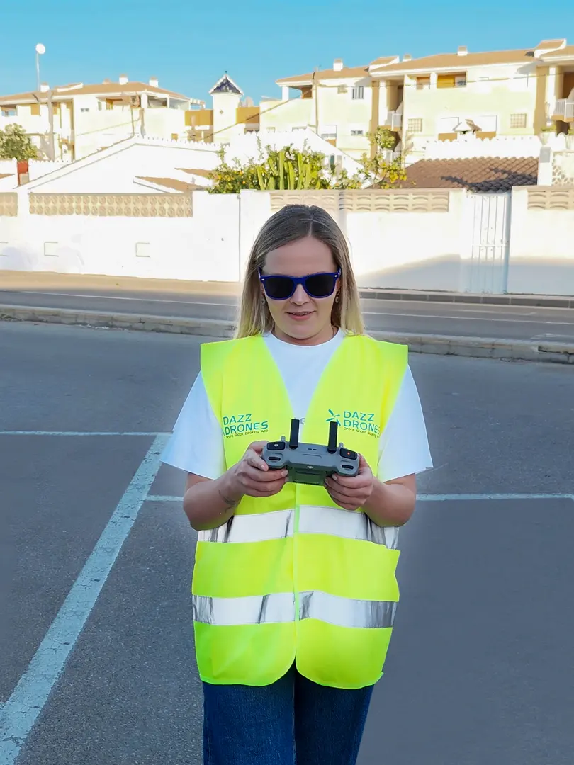 Dazz Drones pilot wearing a high-visibility vest and holding a drone controller on a residential street.