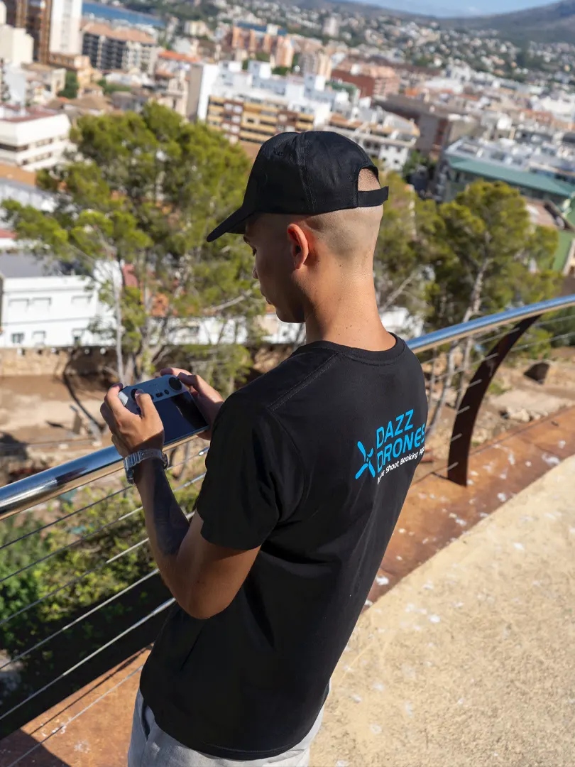 Dazz Drones team member wearing a branded shirt and operating a drone controller overlooking a cityscape.