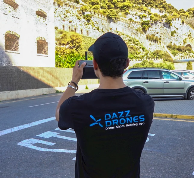 Dazz Drones team member wearing a branded shirt and filming with a smartphone on a street near a historic stone fortress.