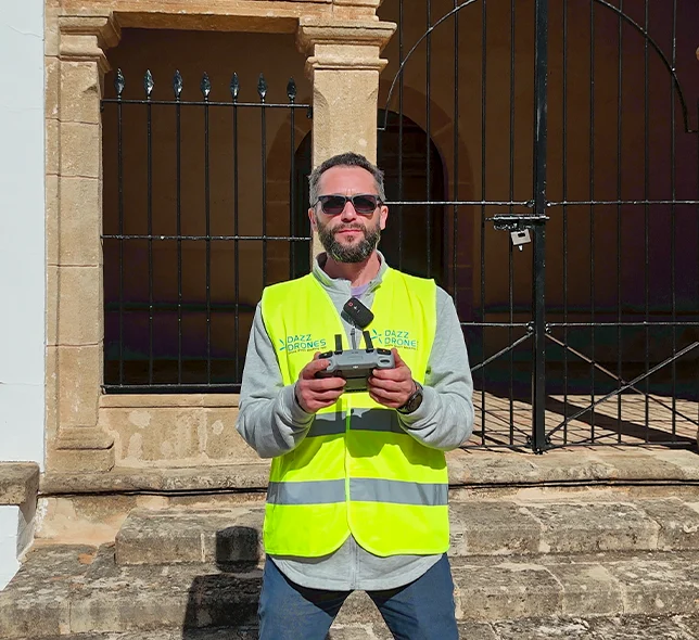 Dazz Drones pilot wearing a high-visibility vest and holding a drone controller in front of a historic building.