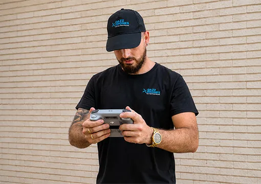Dazz Drones pilot wearing a black cap and T-shirt, operating a drone controller outdoors.