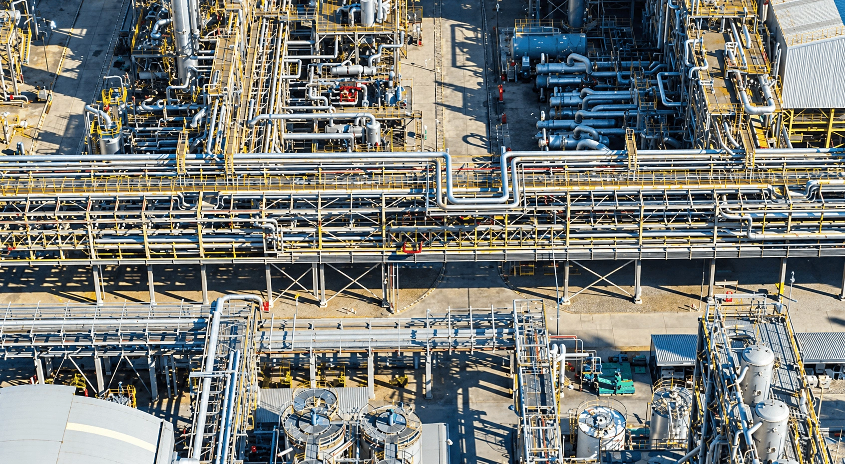 Aerial drone view of an industrial facility with parallel pipelines and utility lines.