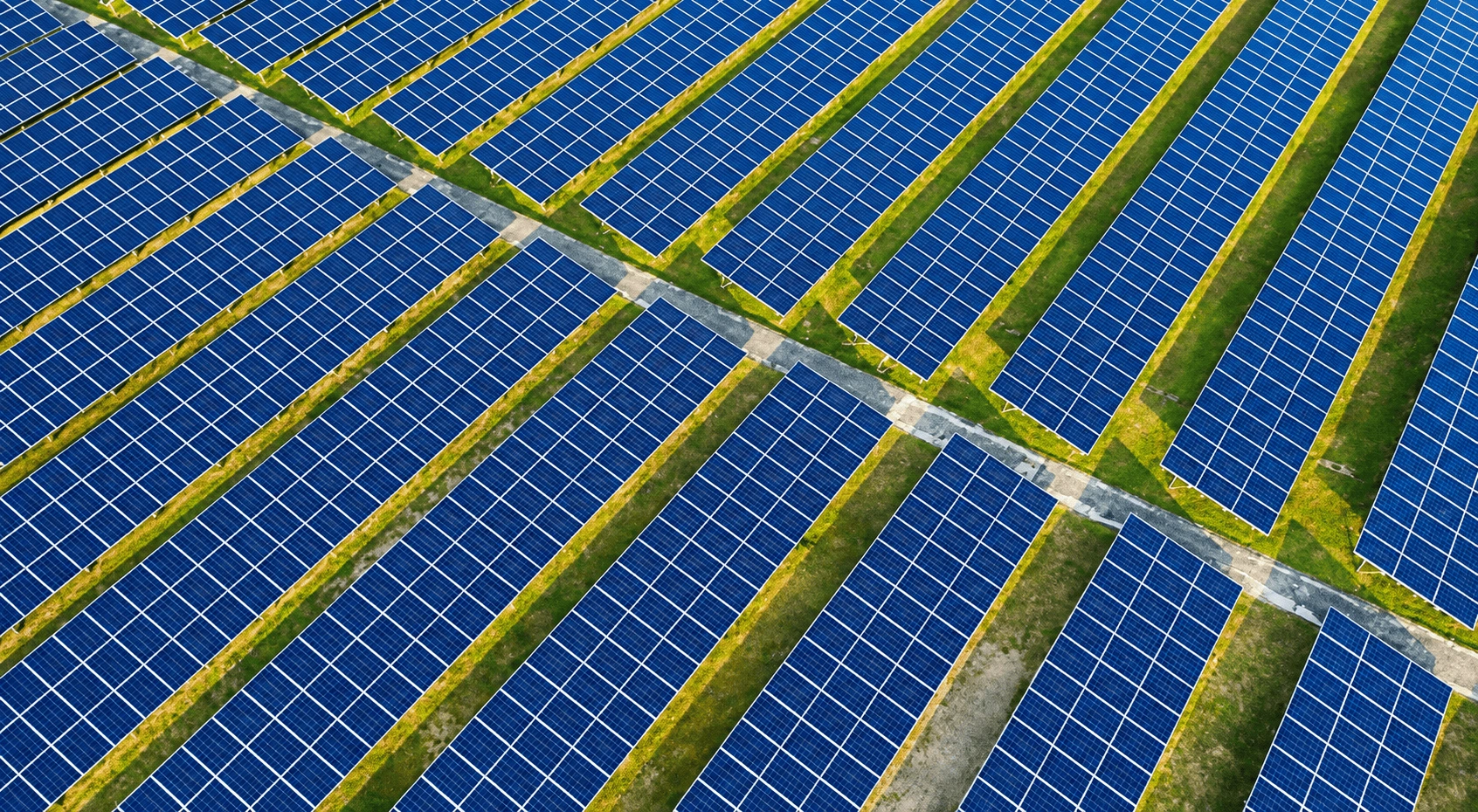 Aerial drone view of rows of solar panels installed across a large open field.