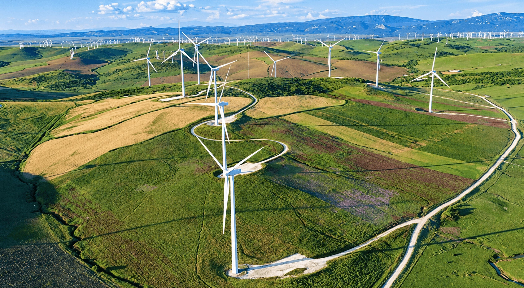 Aerial drone view of a wind farm with multiple wind turbines across agricultural fields.