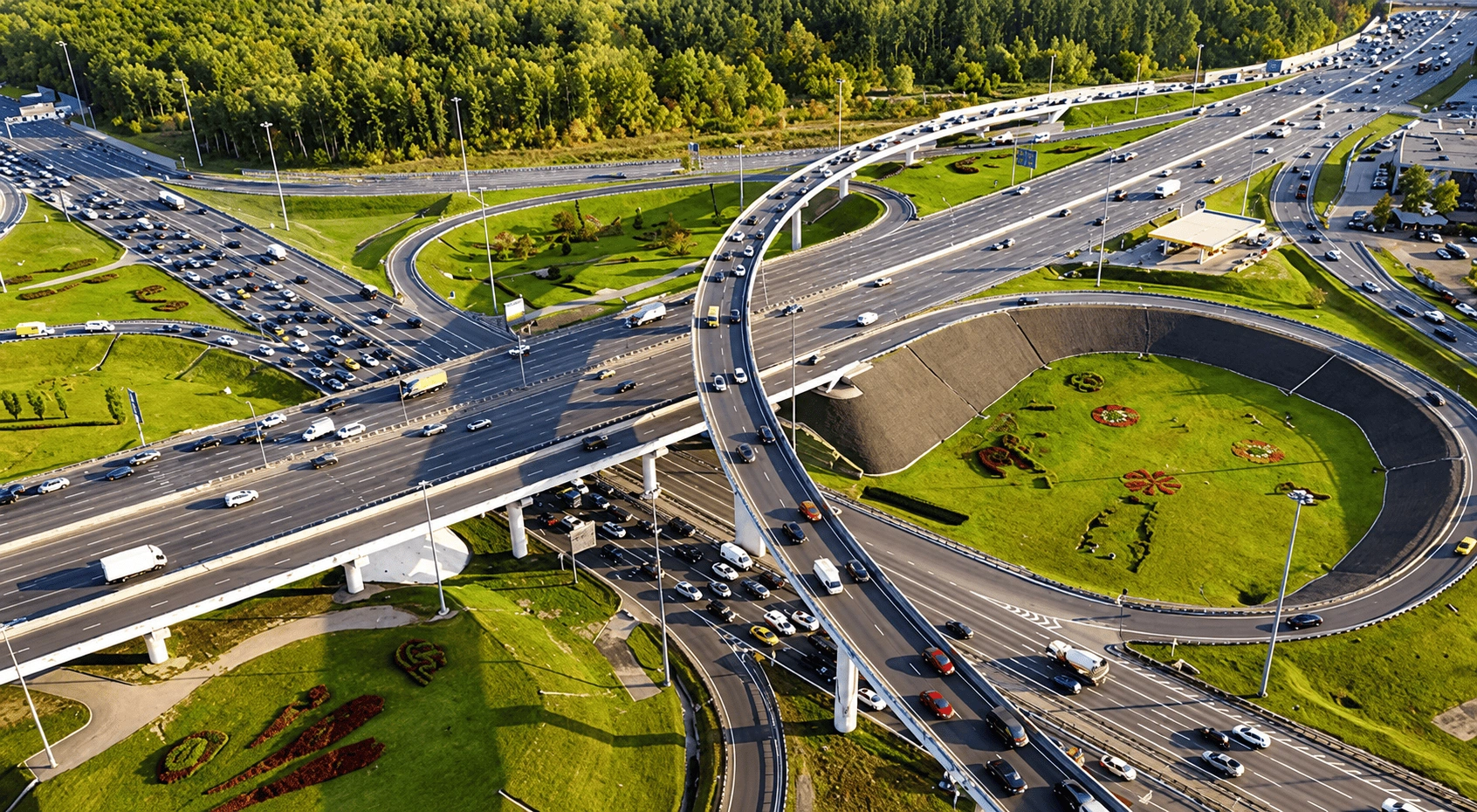 Aerial drone view of a highway interchange surrounded by green fields, roads, and residential areas.