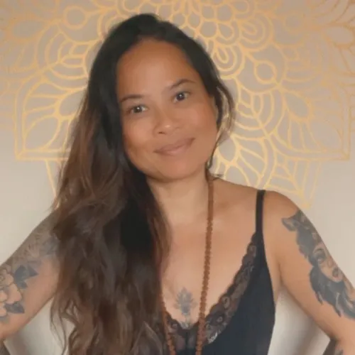 Joy Albano, CAMOH instructor, Woman with long brown hair and tattoos smiling, wearing a black top and necklace, with a decorative gold pattern background.
