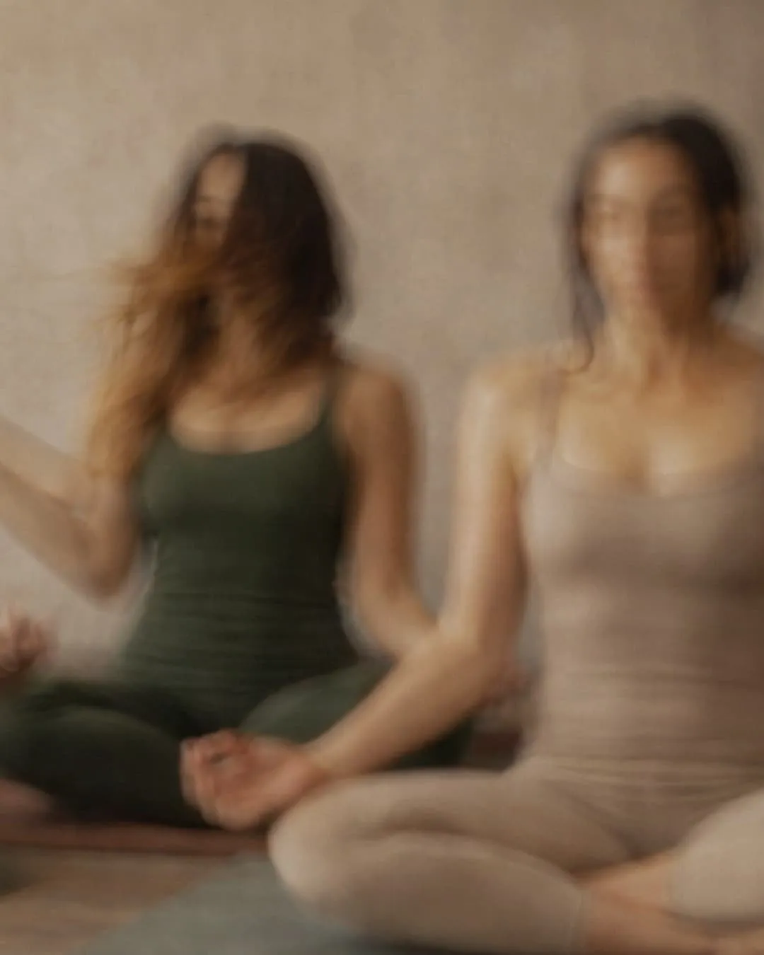 Two women sitting cross-legged in meditation with blurred motion effect.