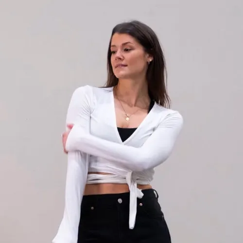 Marie, instructor at CAMOH House in a white wrap top and black pants standing against a neutral background.