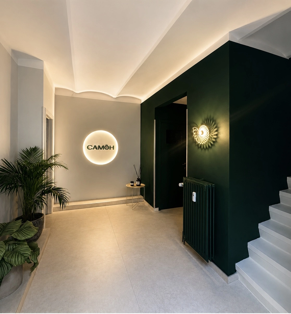 Modern reception area with illuminated CAMÔH sign, green accent wall, plants, and white stairs.