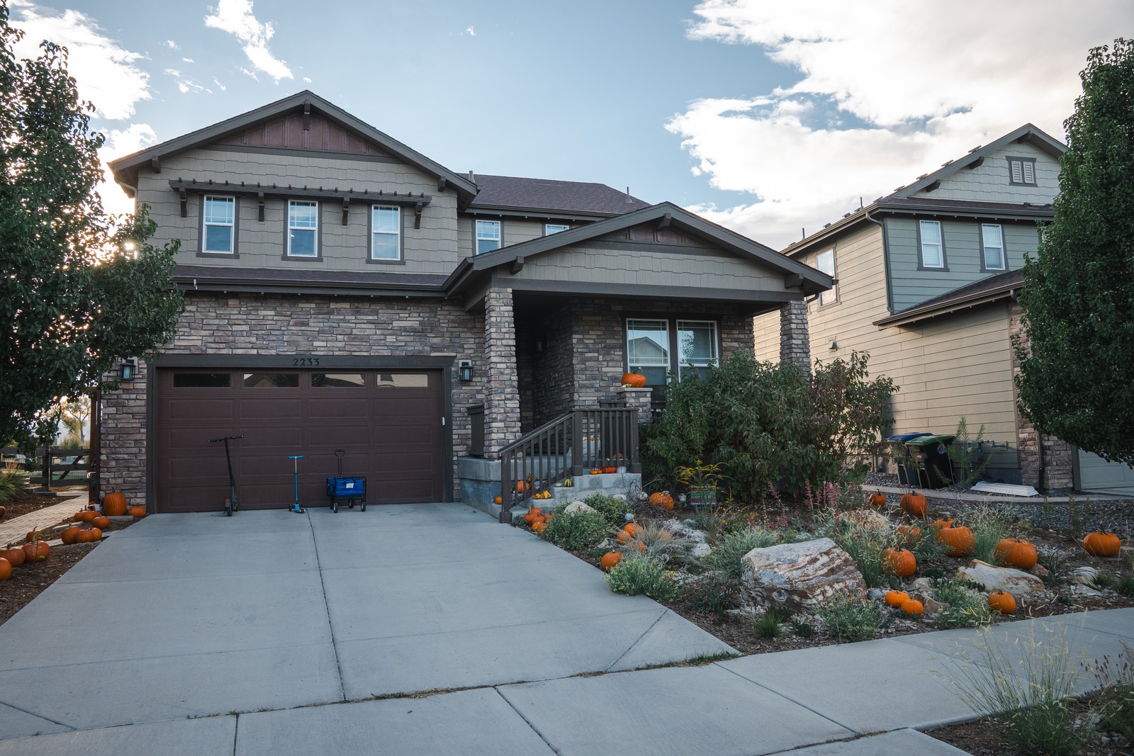 The front of a two-story house with a stone-trimmed entry, a concrete driveway and pumpkins lining the landscaped walkway.