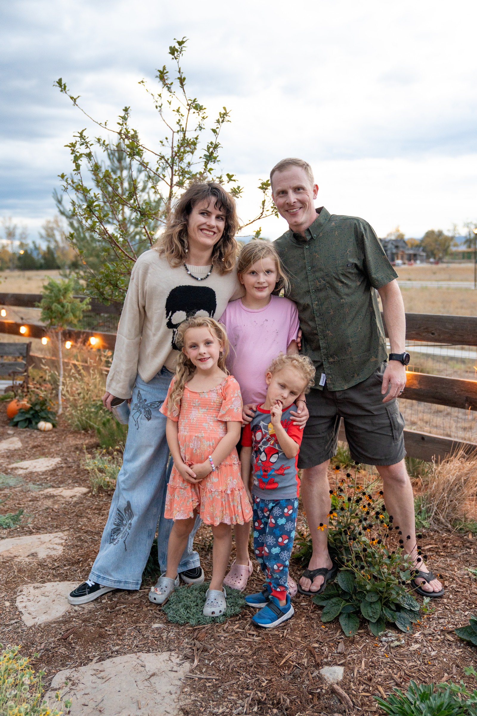 A group poses in a garden with pumpkins and a fence at dusk, smiling at the camera.