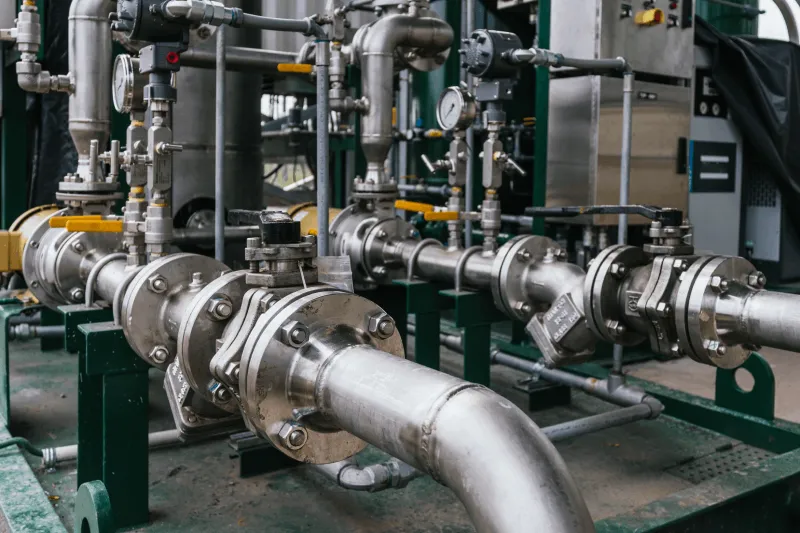 Close-up of stainless steel industrial pipes and valves with pressure gauges in a factory setting.