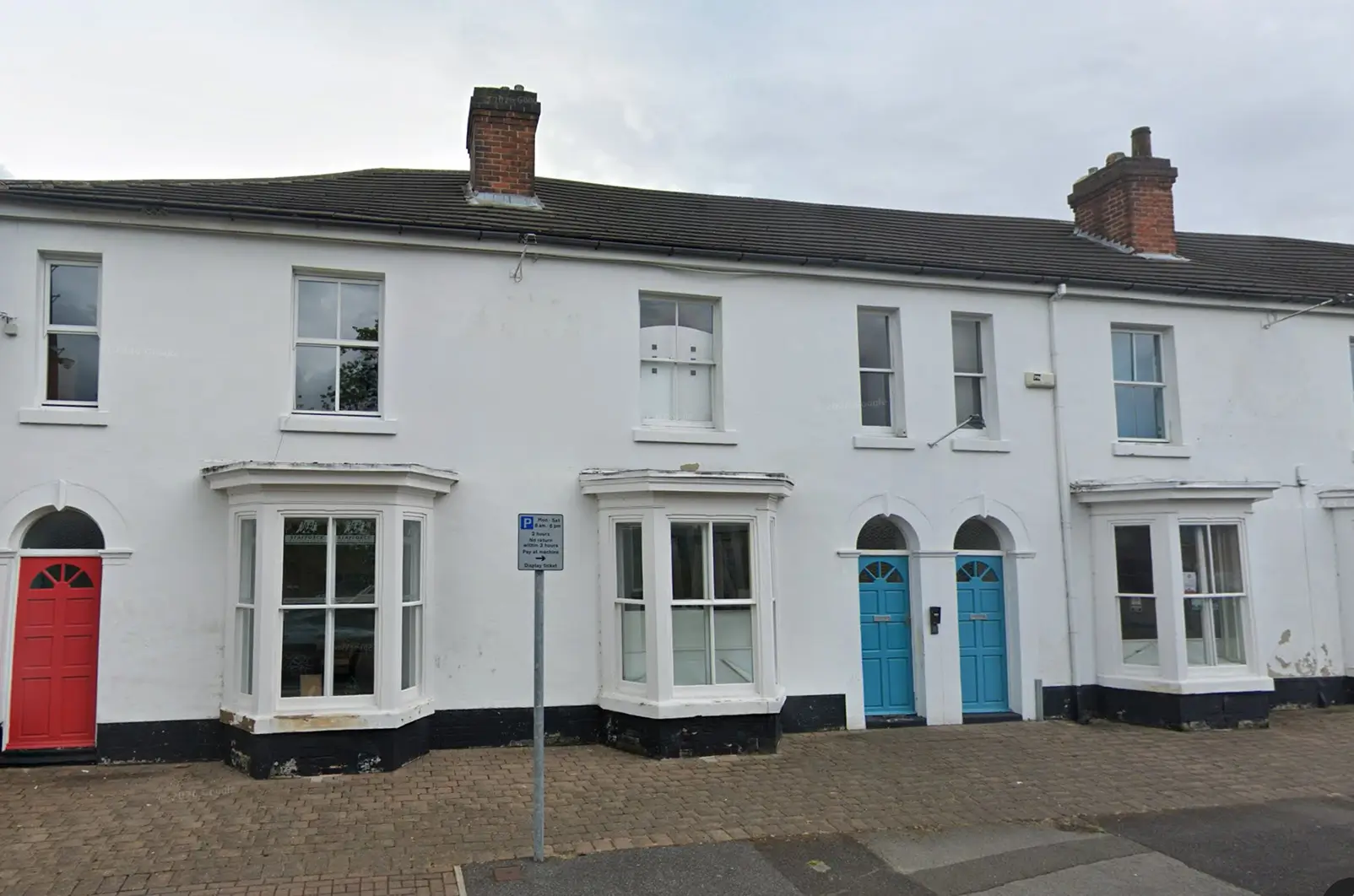 Row of white terraced houses with bay windows and colourful front doors, including red and blue.