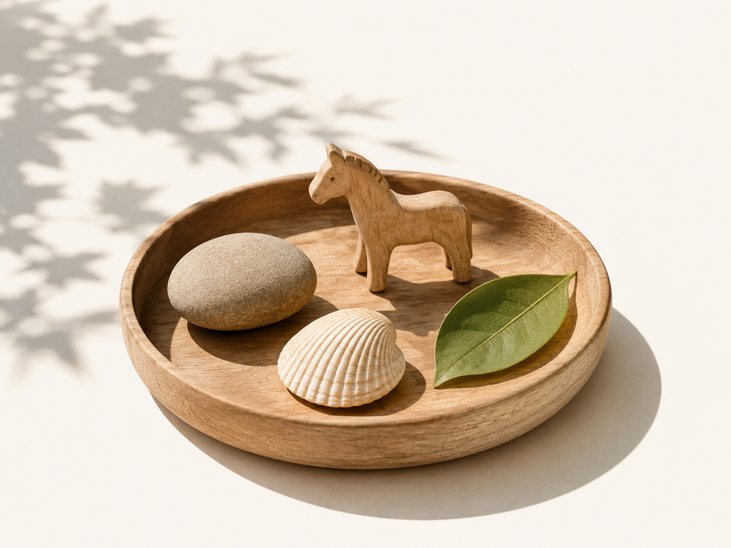 A small wooden tray with a toy horse, stone, shell, and leaf in soft sun and shade