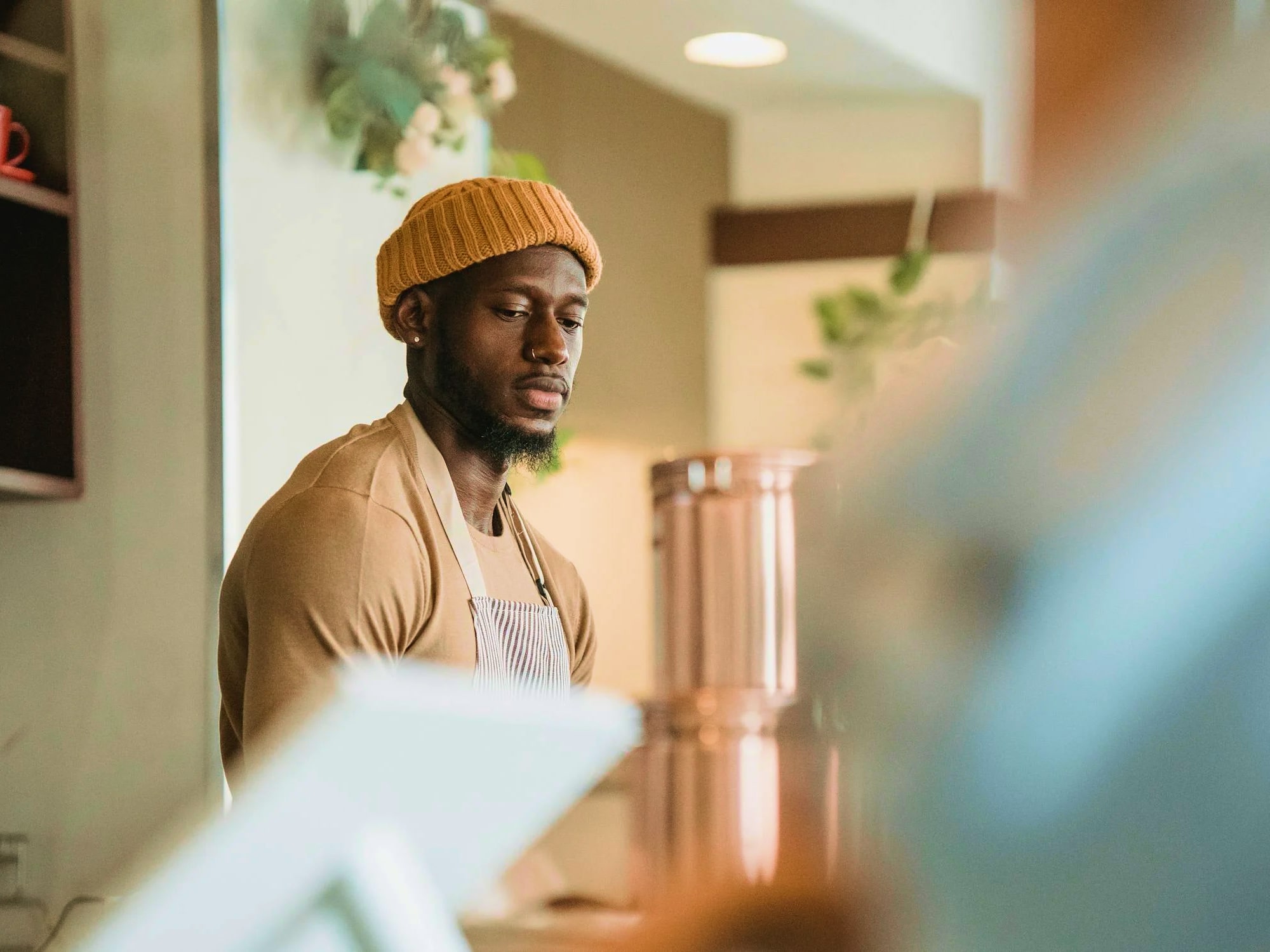 Bearded man in a mustard yellow beanie and apron working behind a counter in a café.