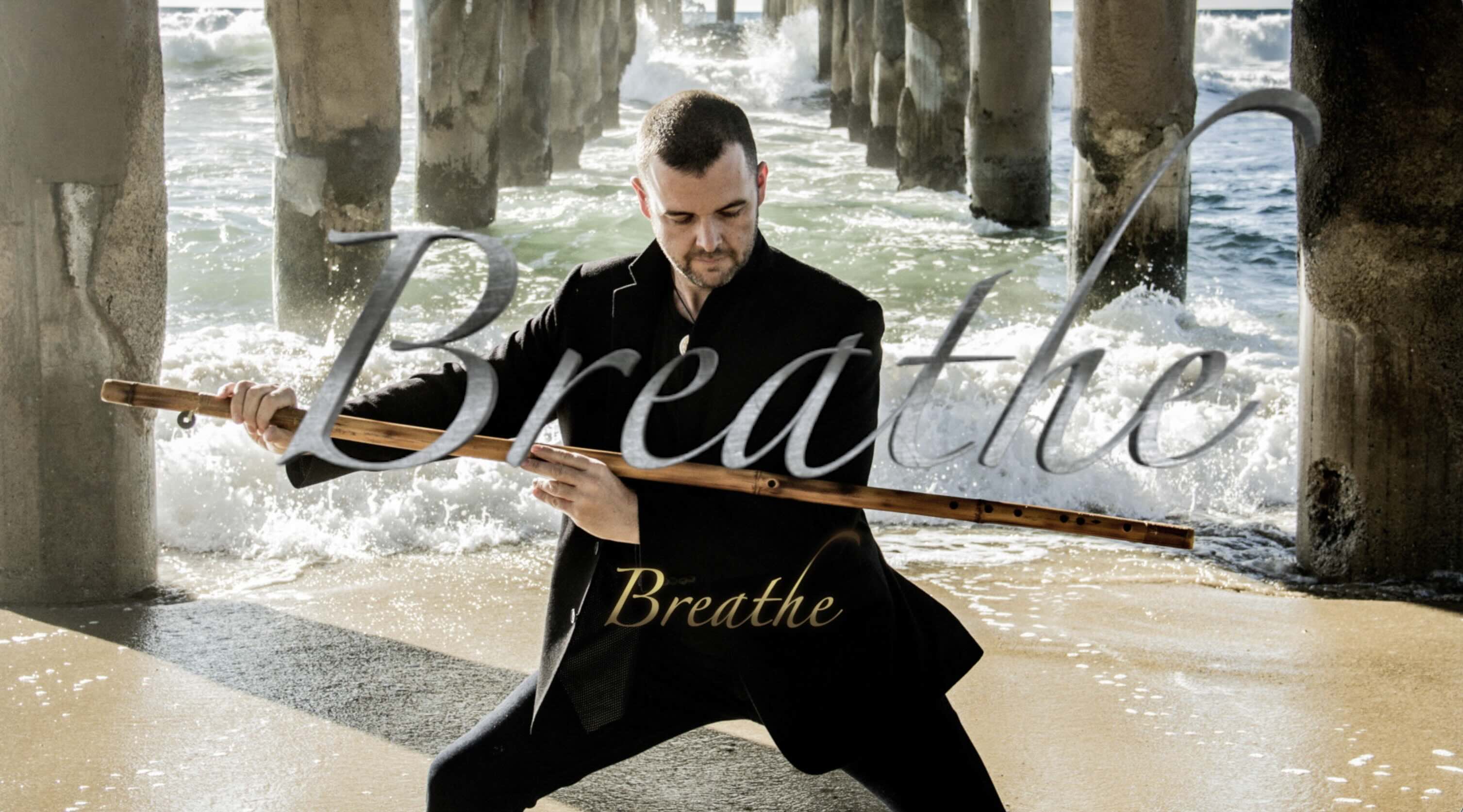 Still image from lyric video man standing in sand beneath peer in yoga pose with long flute