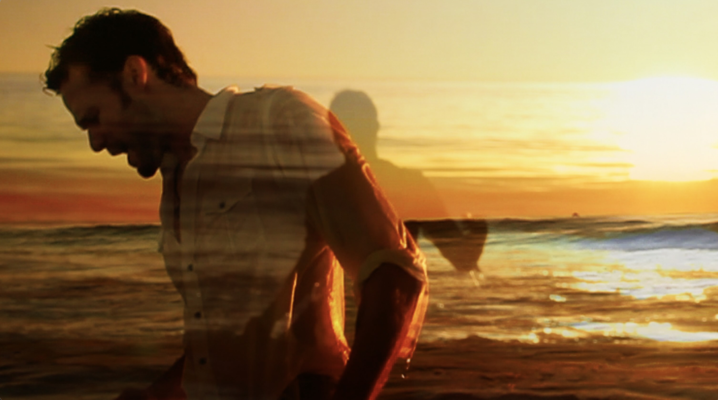 Still from music video man standing in ocean at sunset