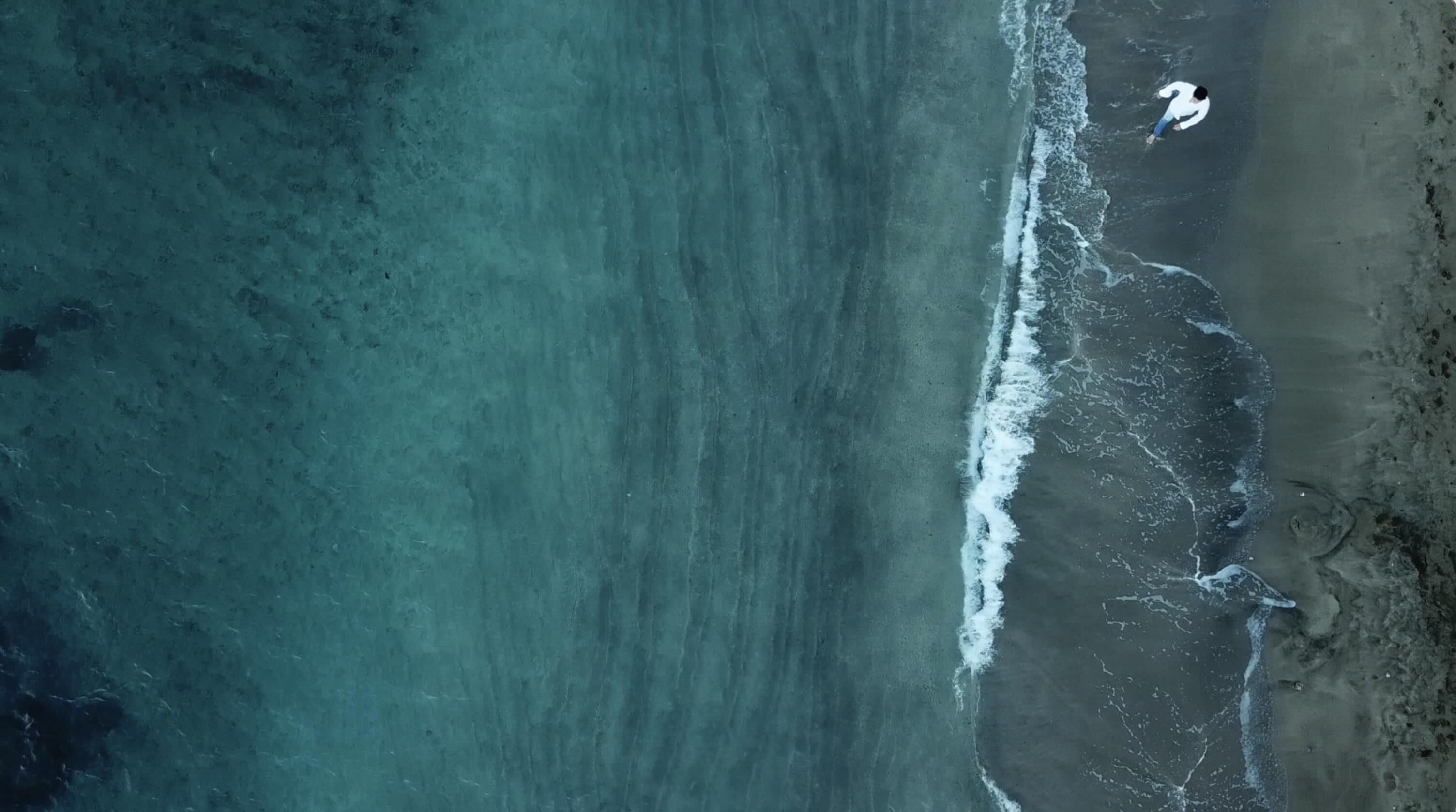 Still image from music video extreme high angle of man walking along beach