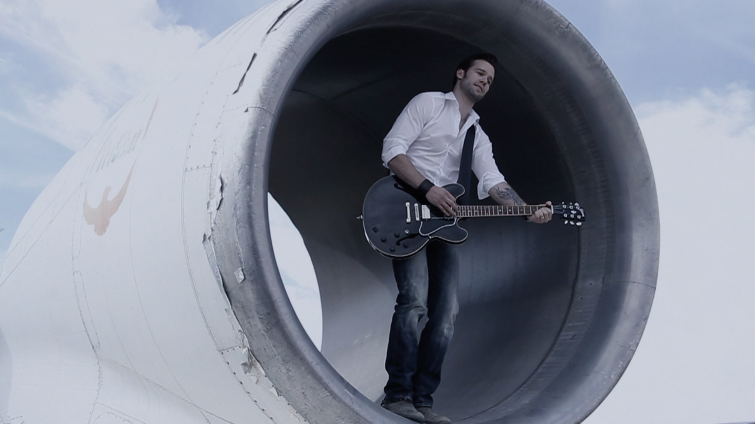 Still image from music video man standing in airplane engine playing guitar