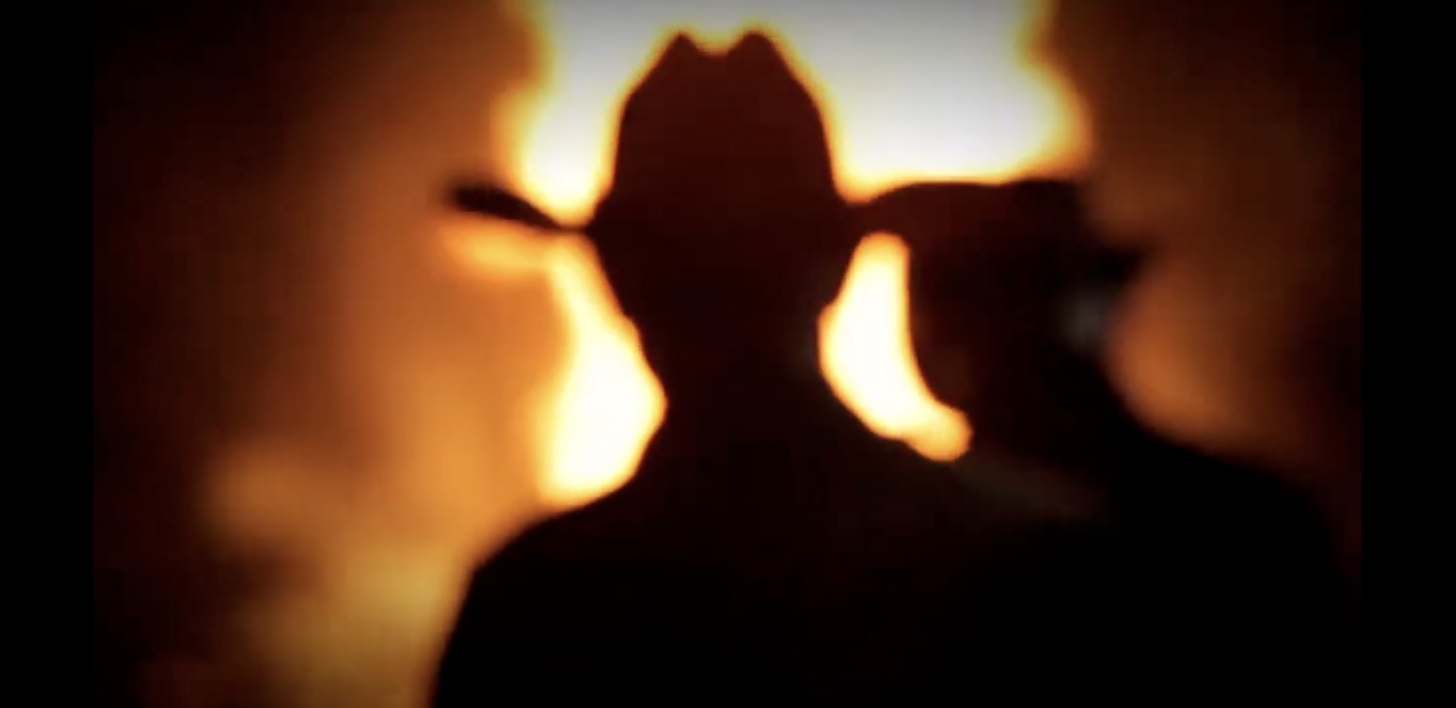 Still image from music video man in silhouette wearing cowboy hat standing in front of bonfire
