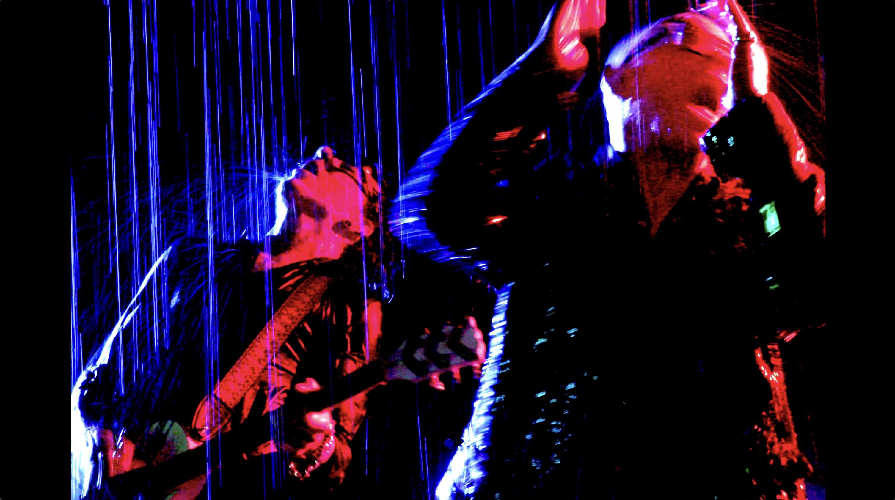 Music video still image two men in red and blue colored lights rain pouring down on them