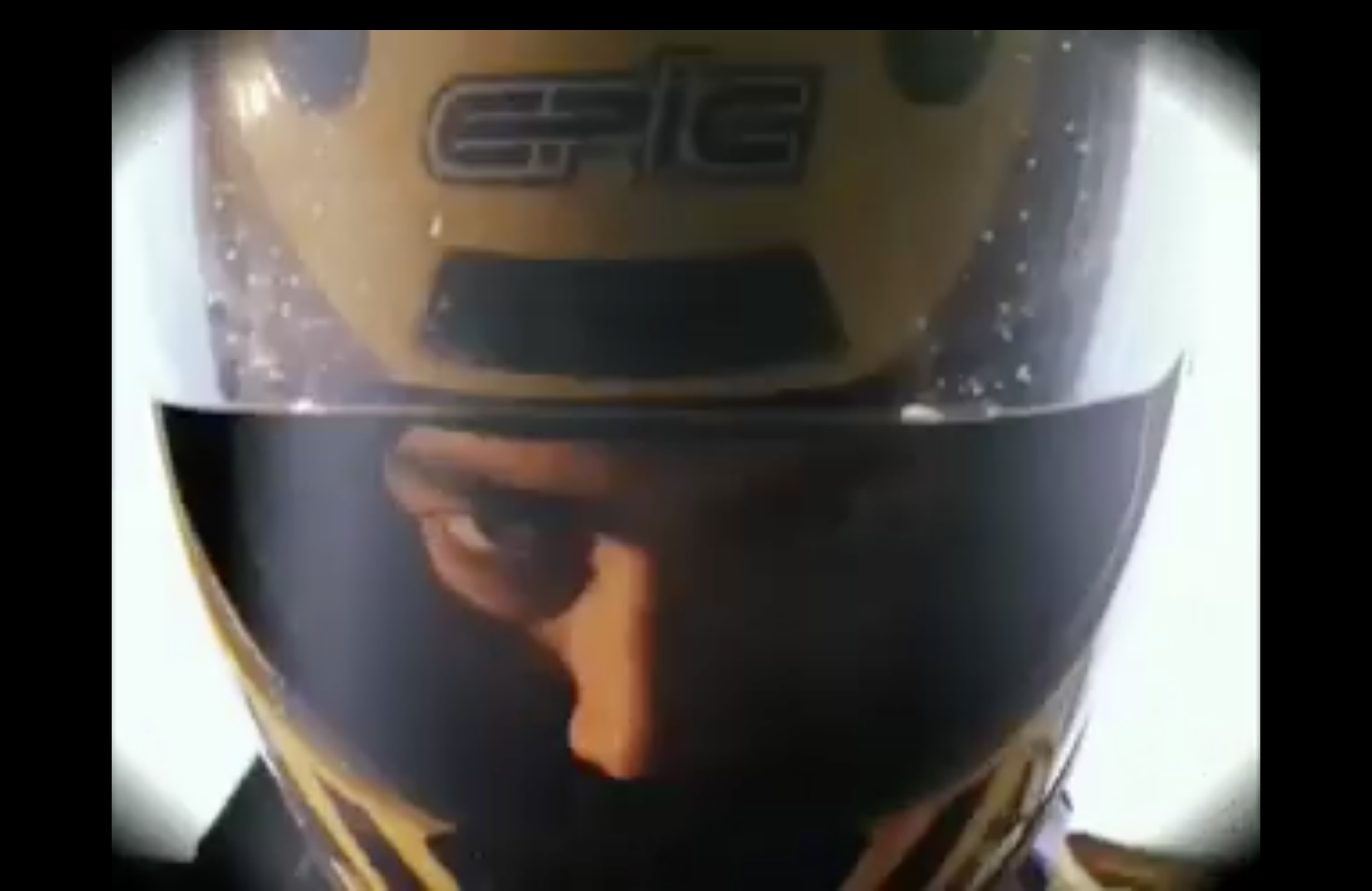 Close up of a man wearing a yellow and black motorcycle helmet still image from music video